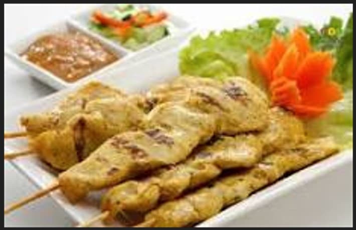 Grilled chicken satay skewers served with peanut sauce, cucumber salad, and a carved carrot flower.